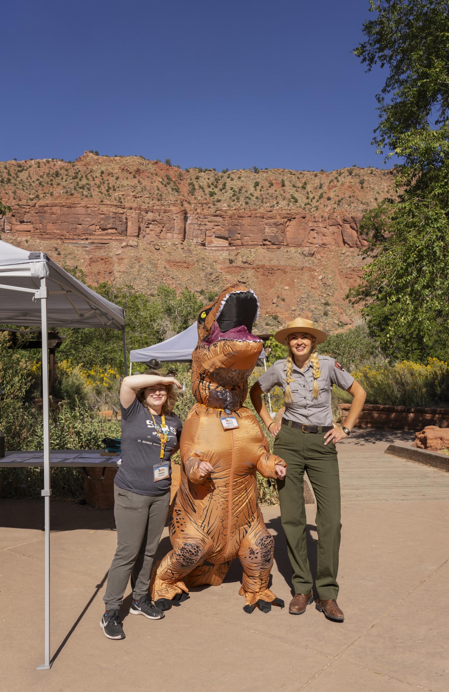 Two park rangers with inflatable dinosaur in desert setting.