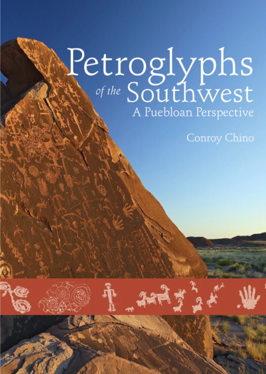 Petroglyph-covered rock under blue sky in a desert landscape.