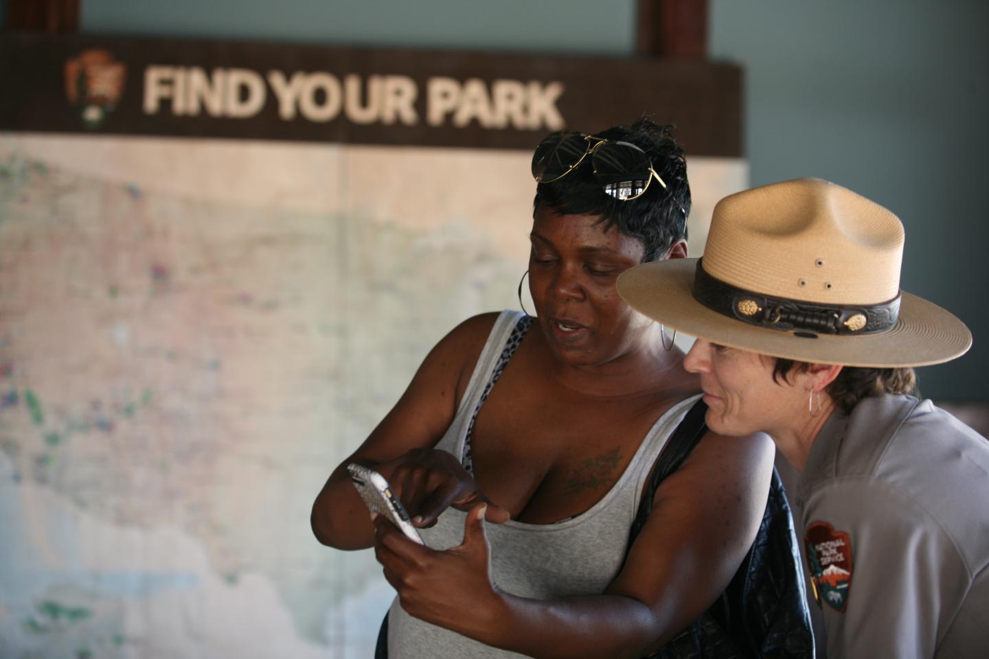 Woman and park ranger looking at a phone with a map in the background.