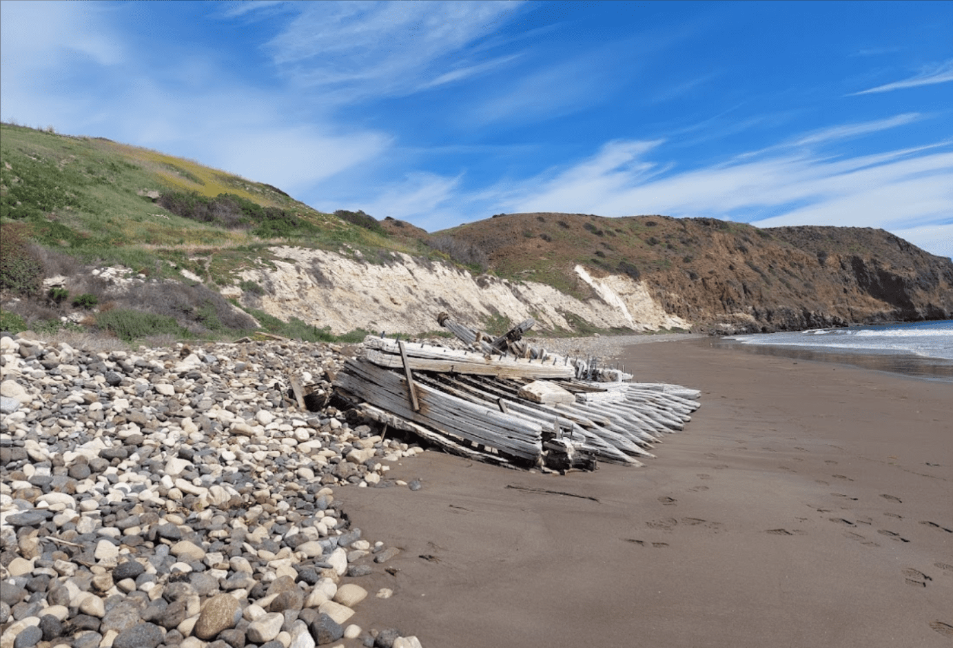 Driftwood shelter on a rocky beach under a bright blue sky.
