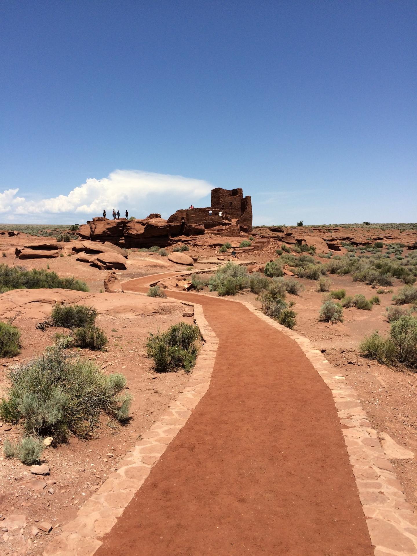 Desert path leading to ancient ruins under a clear blue sky.
