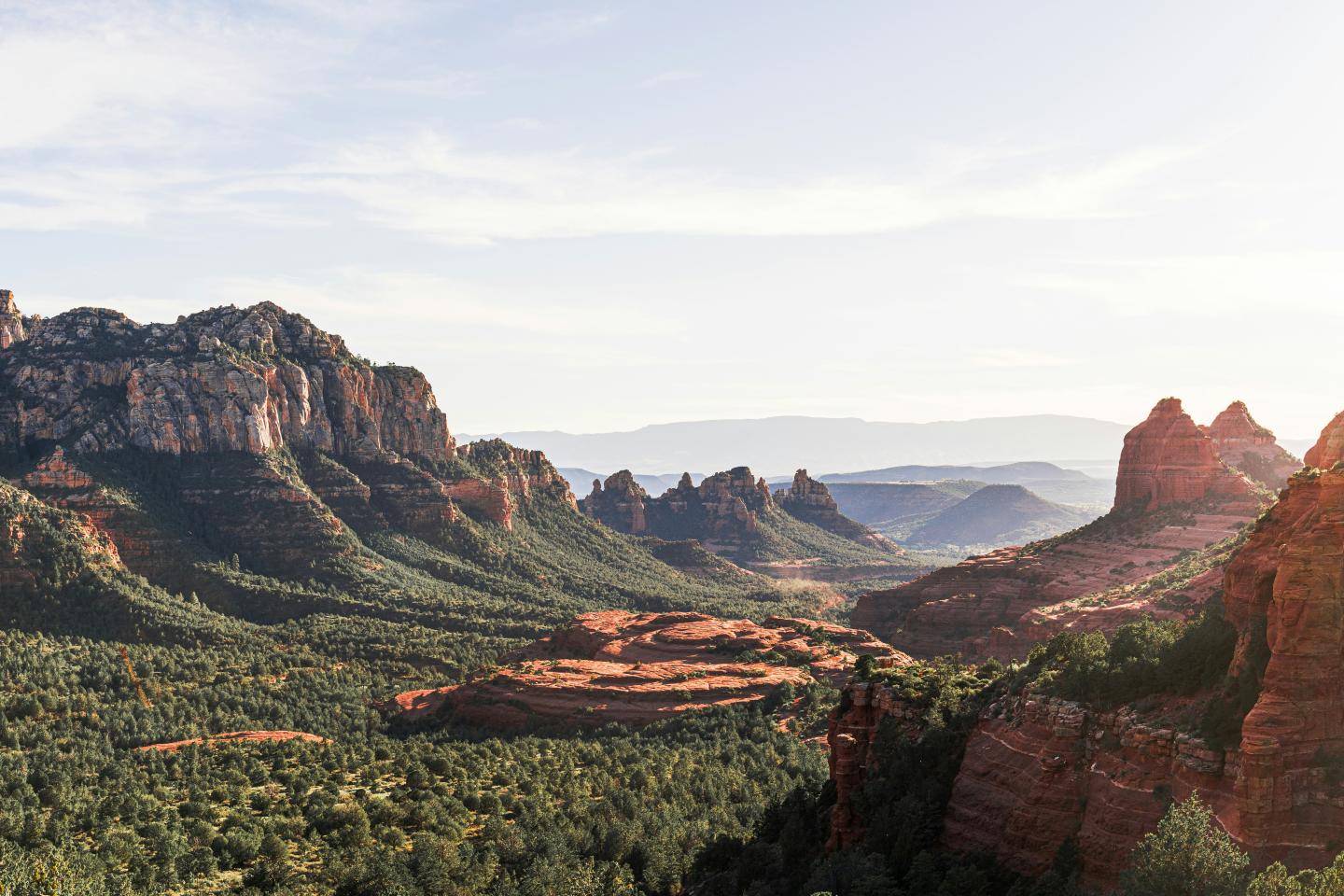 Red rock formations and green forest under a bright sky.