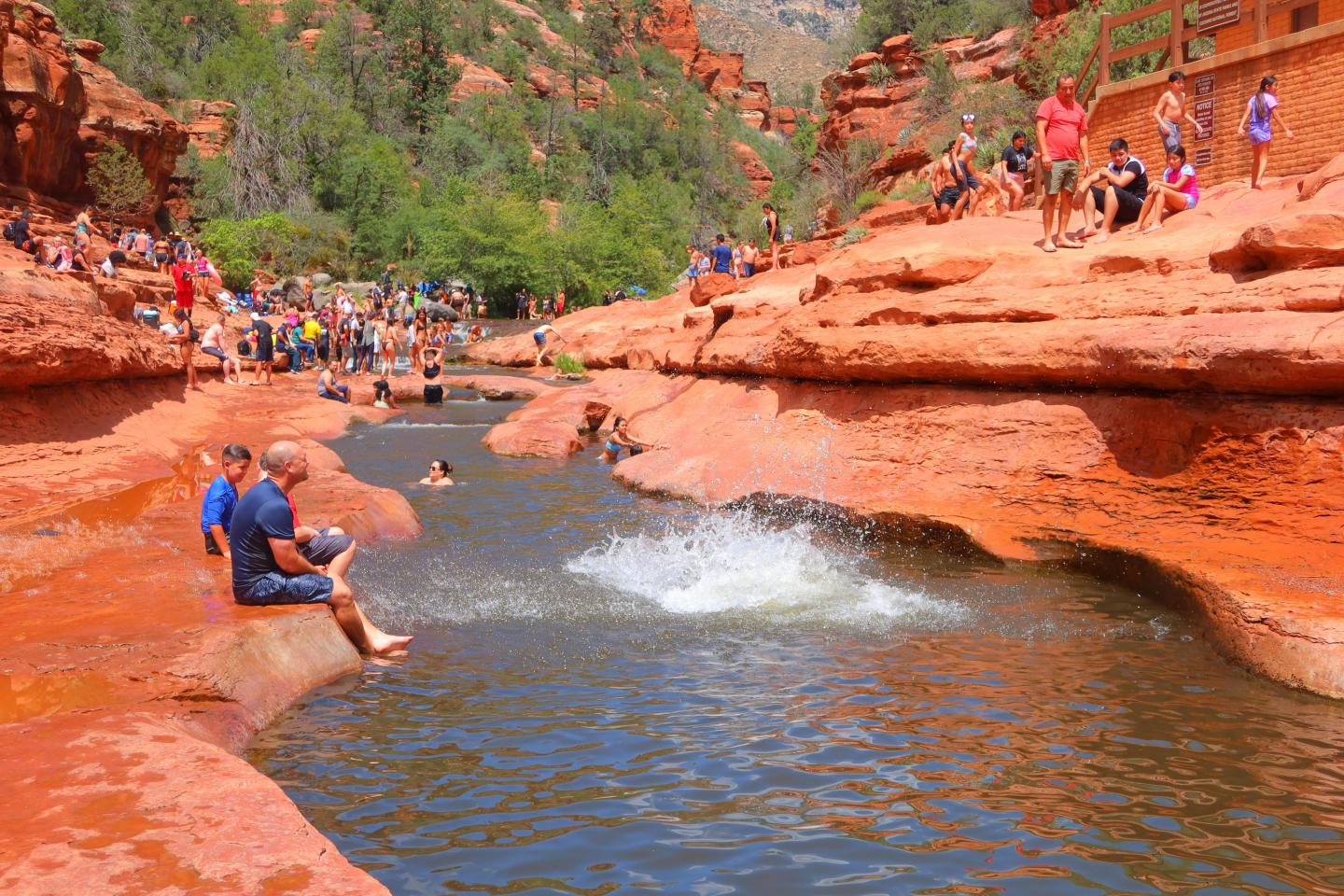 People enjoying a natural water slide in a rocky, red canyon.