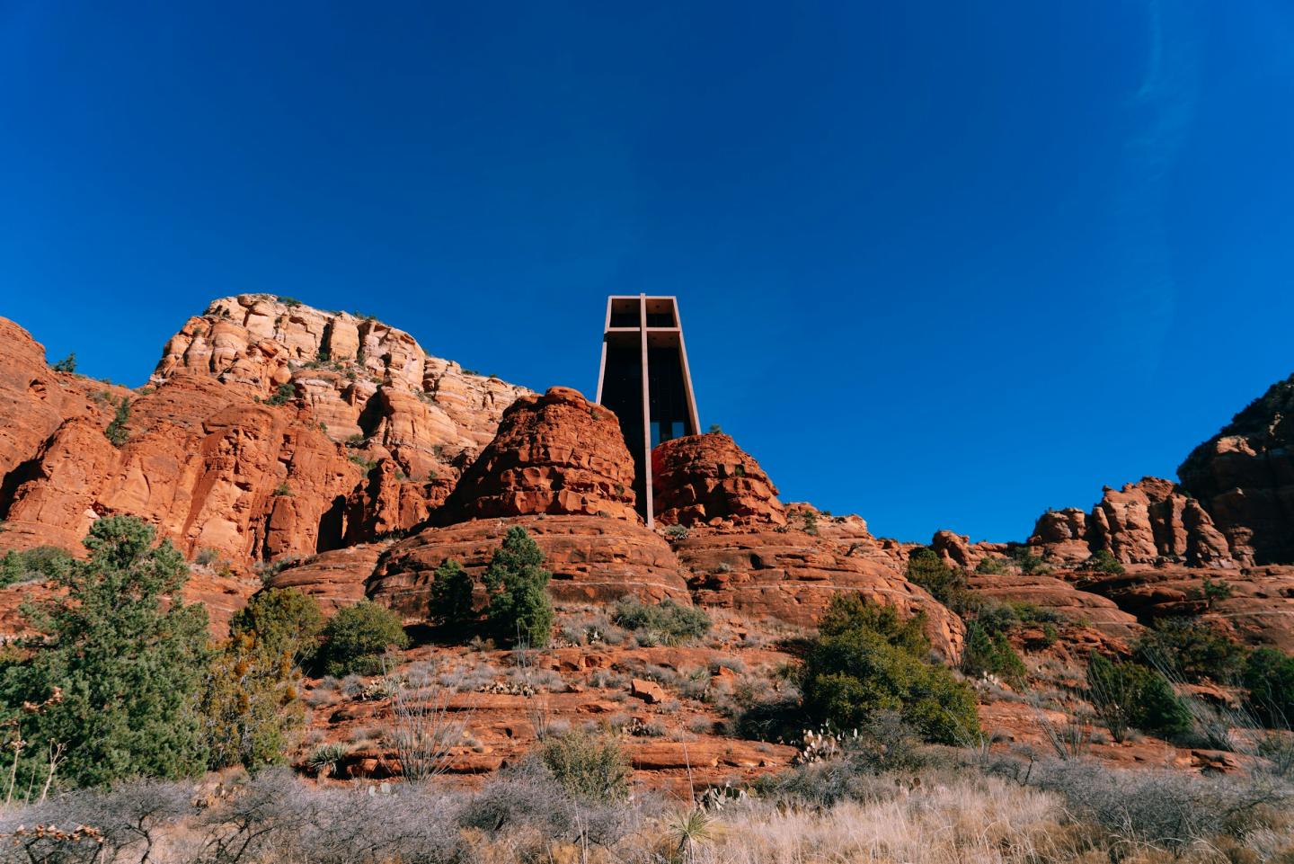 Rust-colored rock formations under a clear blue sky with a chapel embedded in the rocks.