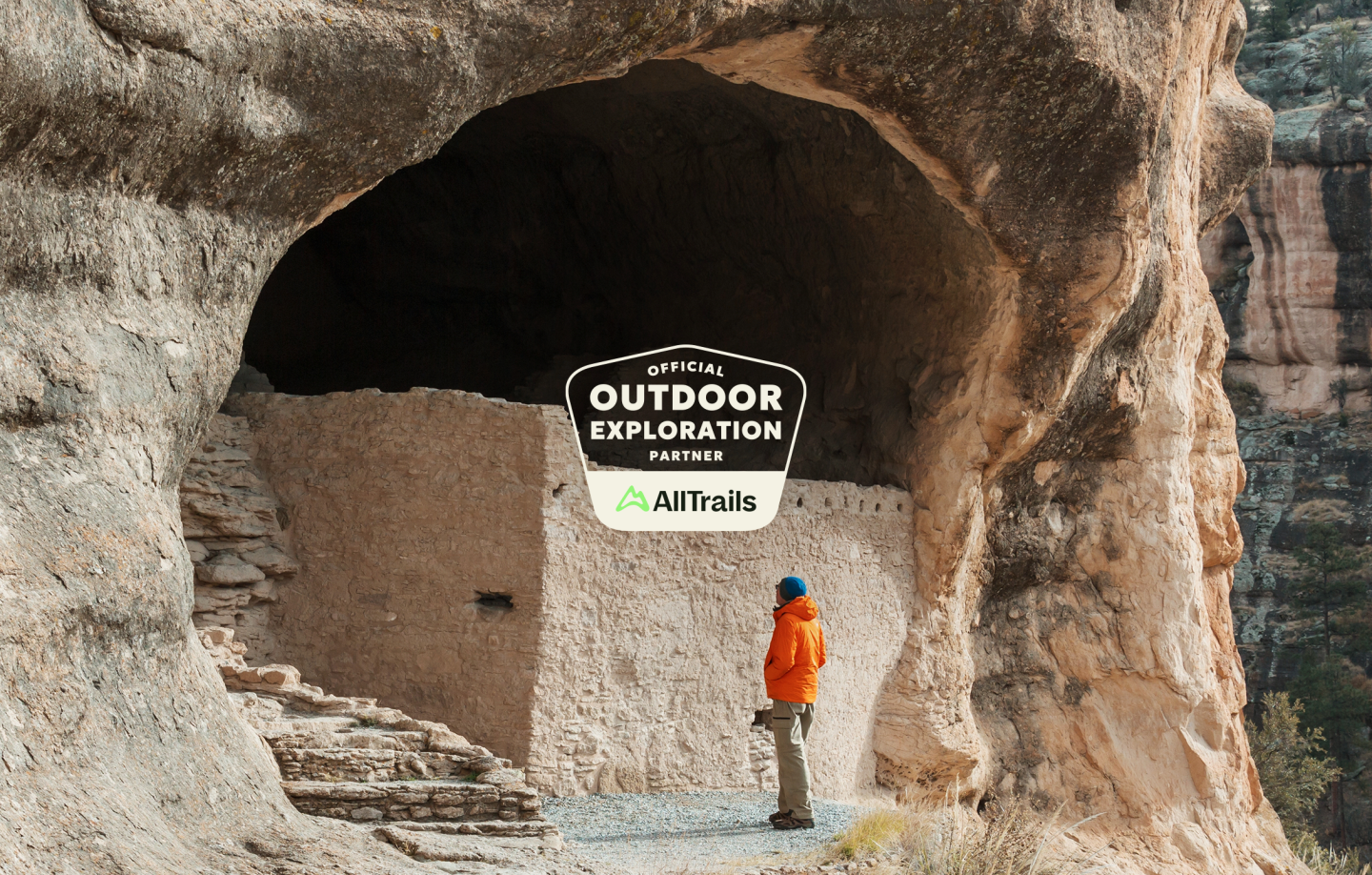 Cliff dwelling with a person in an orange jacket standing nearby.