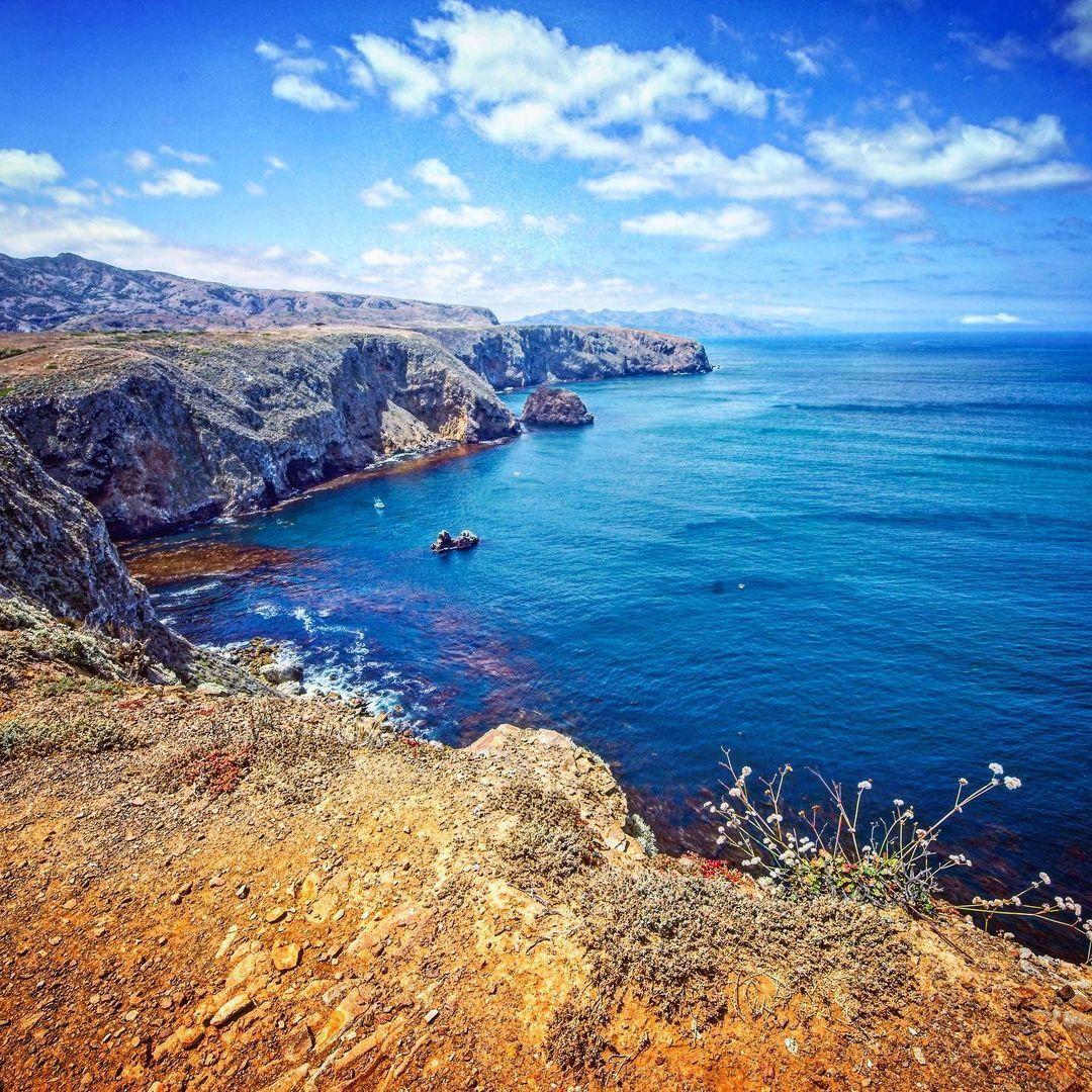 Cliffside view over a blue ocean under a bright sky with scattered clouds.