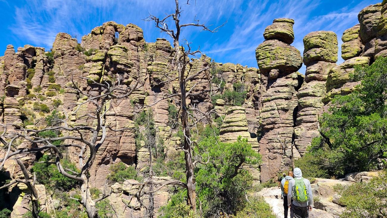 Hiker approaching towering rock formations under a clear blue sky.