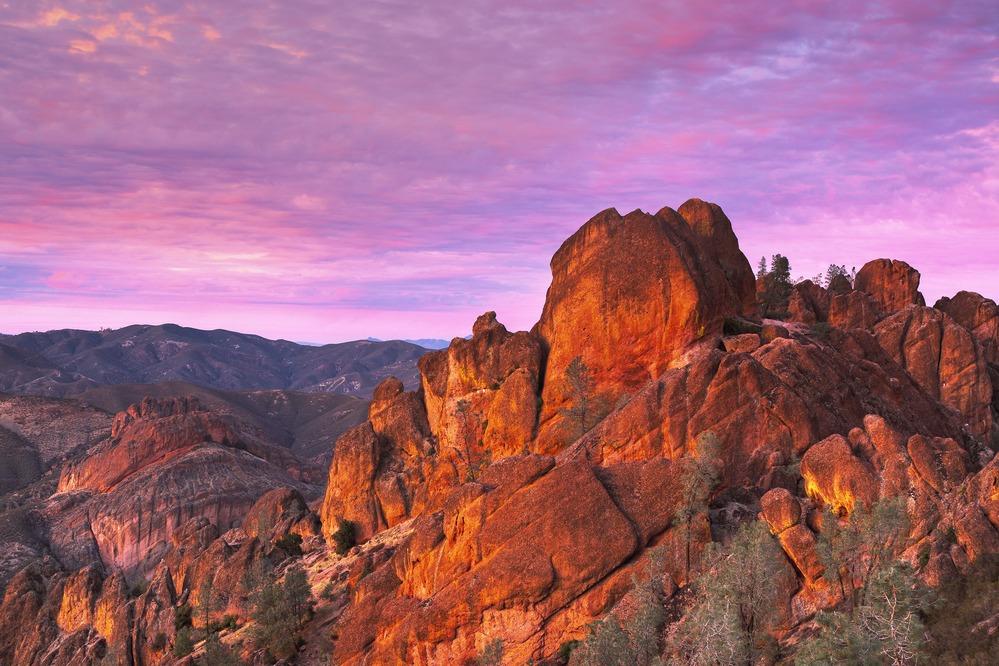 Reddish rocky cliffs under a pink and purple sunset sky.