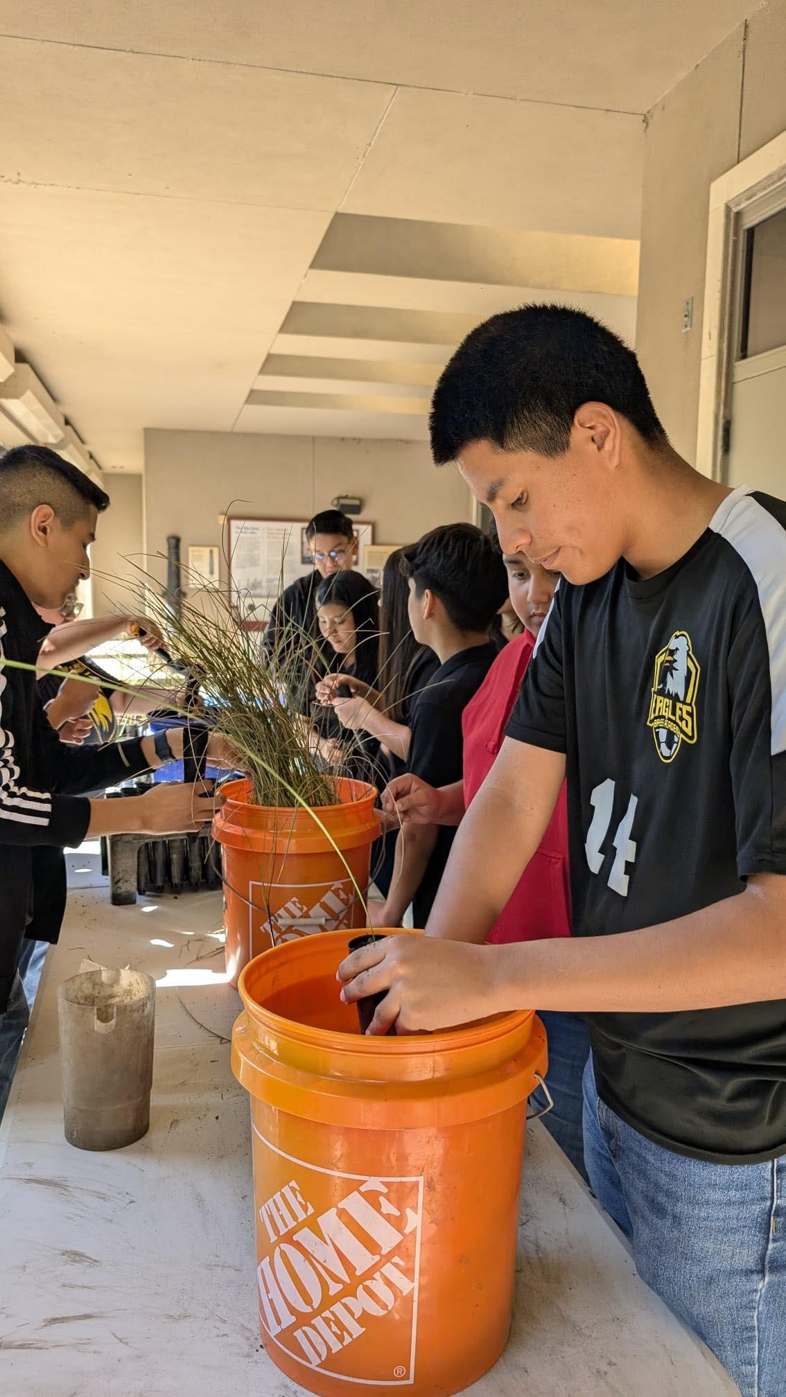 People planting in orange buckets under a covered outdoor area.