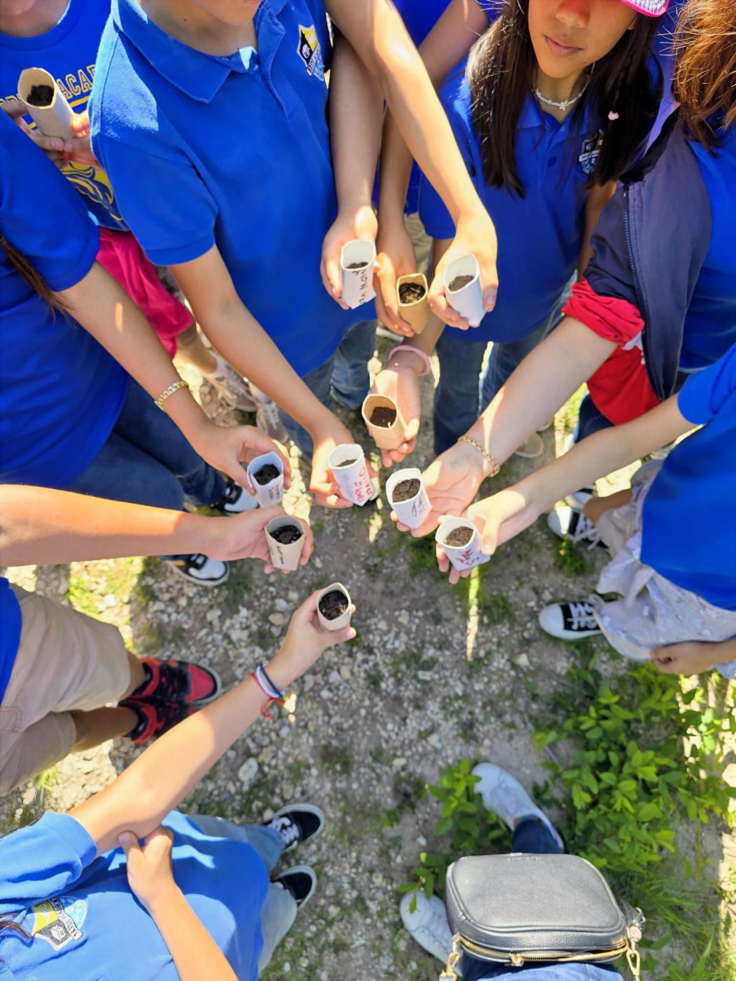 Group holding small potted plants in an outdoor setting, wearing blue shirts.