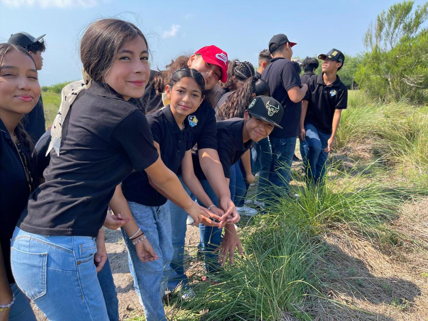 Group of people in black shirts outdoors examining grass.