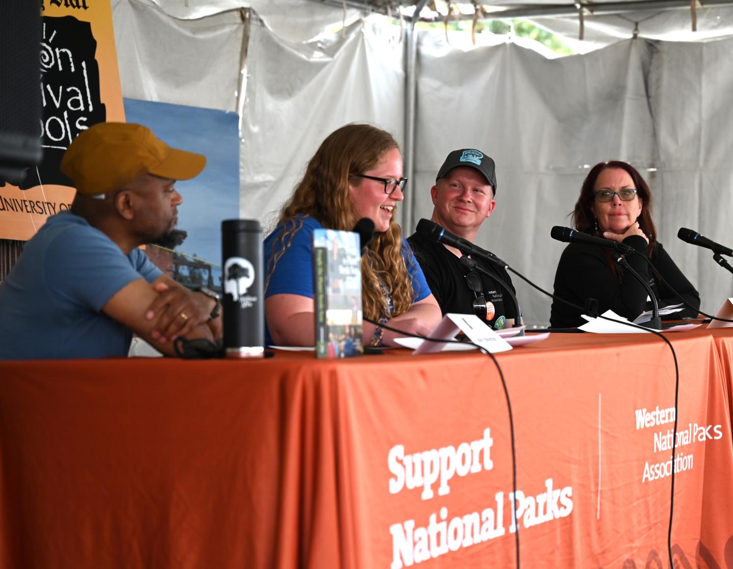 Panel discussion with four people, an orange tablecloth, and microphones in a tent.