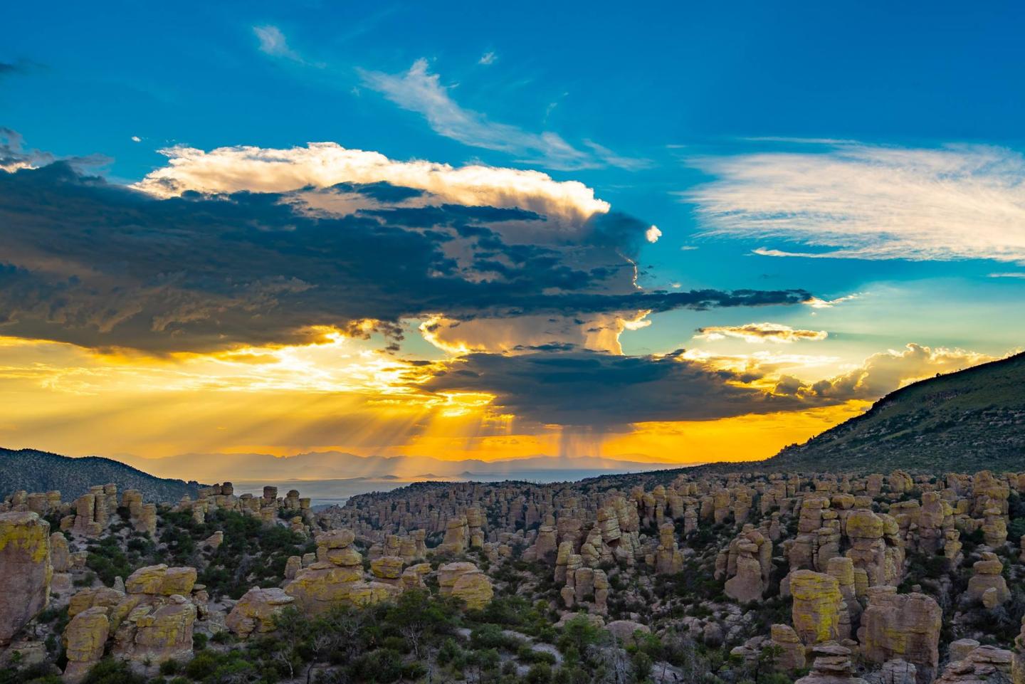 Dramatic sunset over a desert landscape with rock formations and vibrant sky.