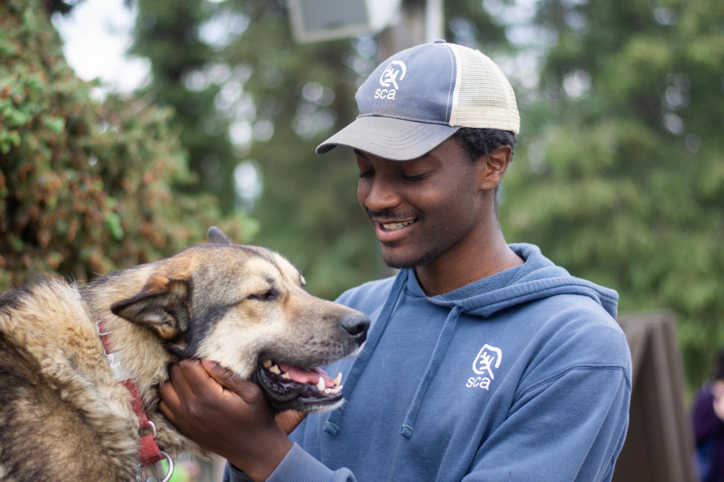 Young man gently holding a large dog outdoors, both appear happy.