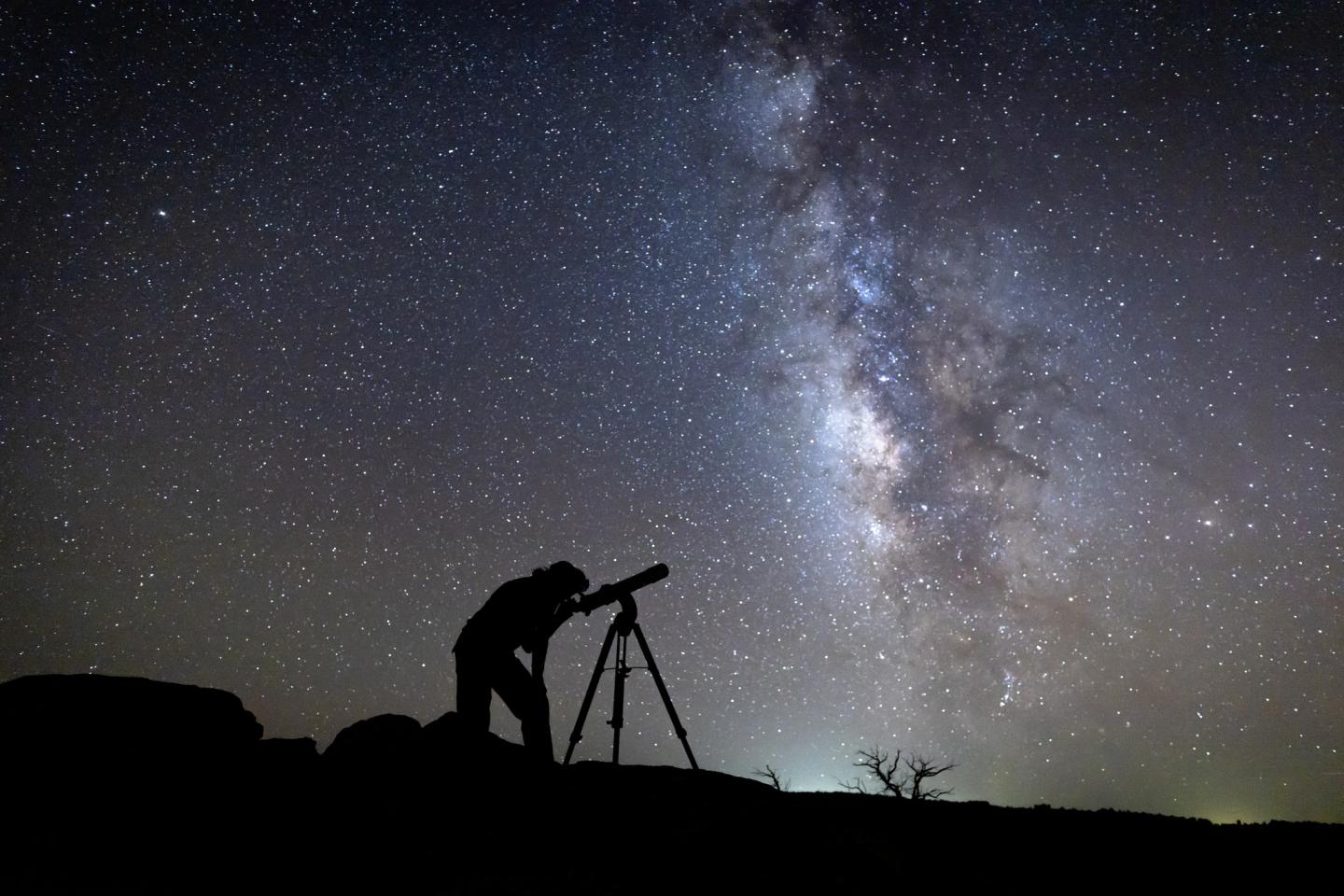 Silhouette of person using a telescope under a starry sky with the Milky Way.