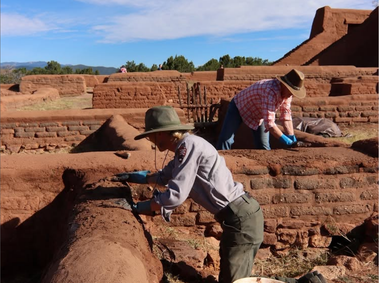 Archaeologists restoring ancient brick ruins under a clear blue sky.