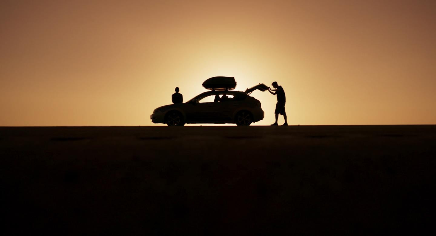 Silhouette of people loading a car at sunset.