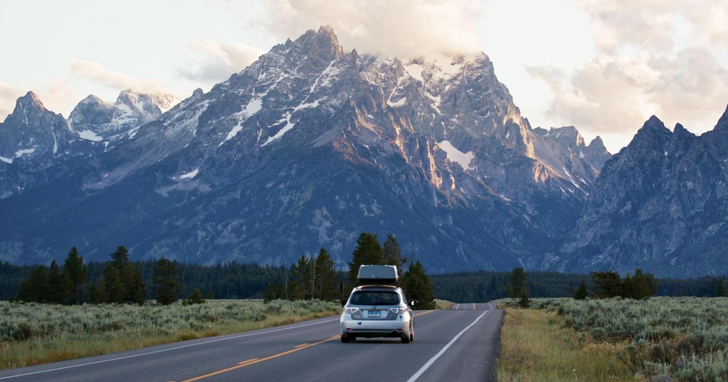 Car on road approaching majestic snow-capped mountains.