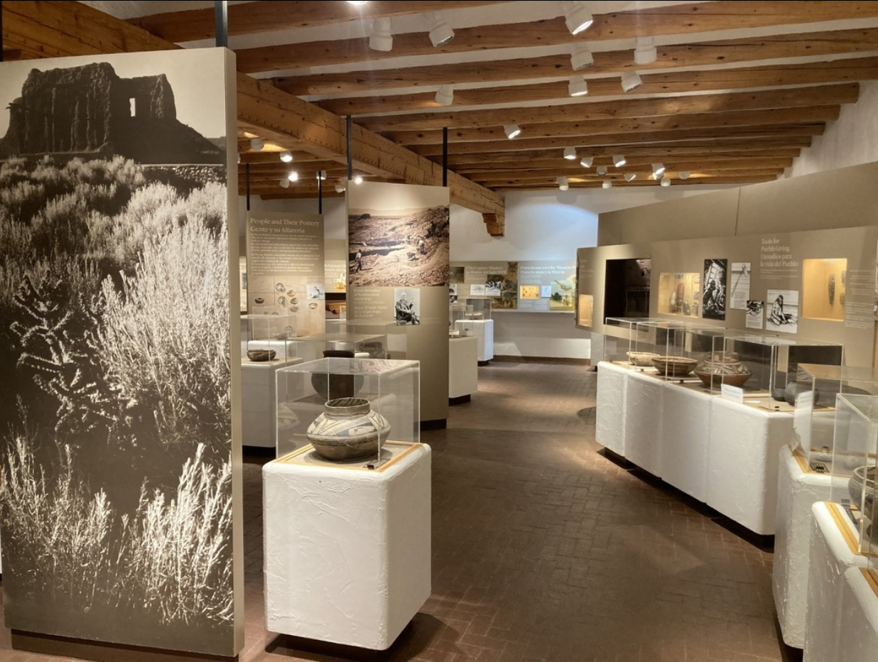 Museum exhibit with displays and large photograph, wood-beamed ceiling.
