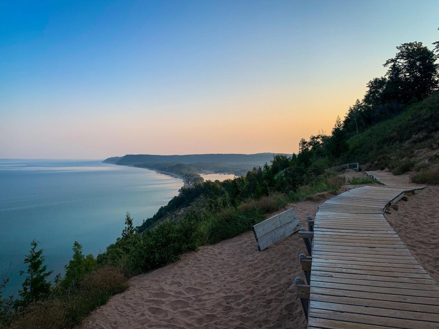 Coastal boardwalk at sunset with serene water and lush greenery.