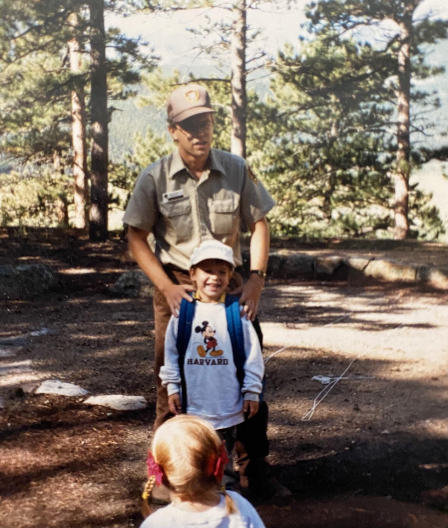 Ranger with two children in a forest setting, sunlight filtering through trees.