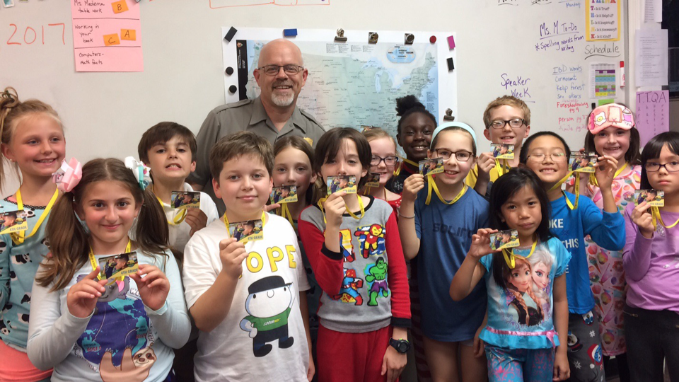 Smiling children with a teacher, holding lanyards in a classroom setting.