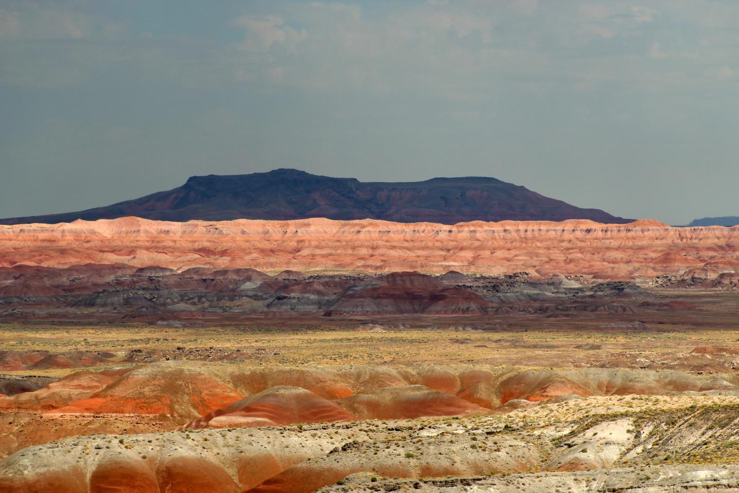 Desert landscape with layered red and orange rock formations under a cloudy sky.