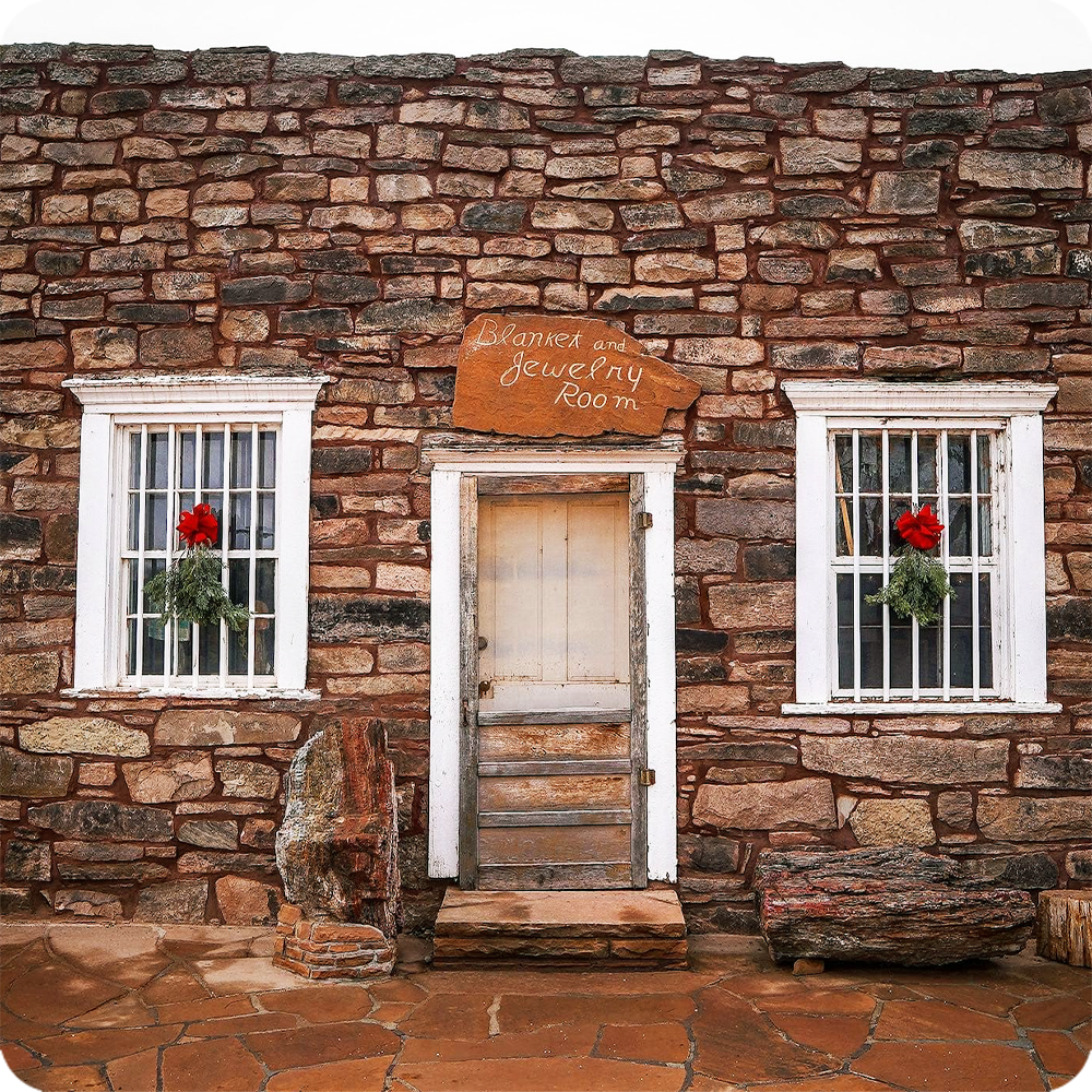 Rustic stone building with white windows, wreaths, and a wooden door.