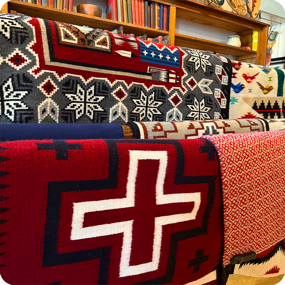 Colorful woven blankets with geometric patterns displayed on shelves.