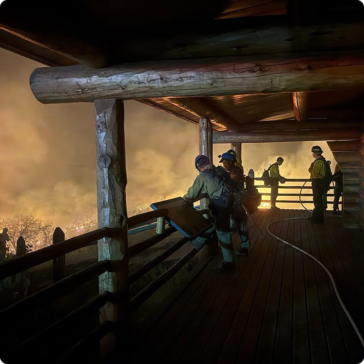 Firefighters on a wooden porch watching a wildfire.