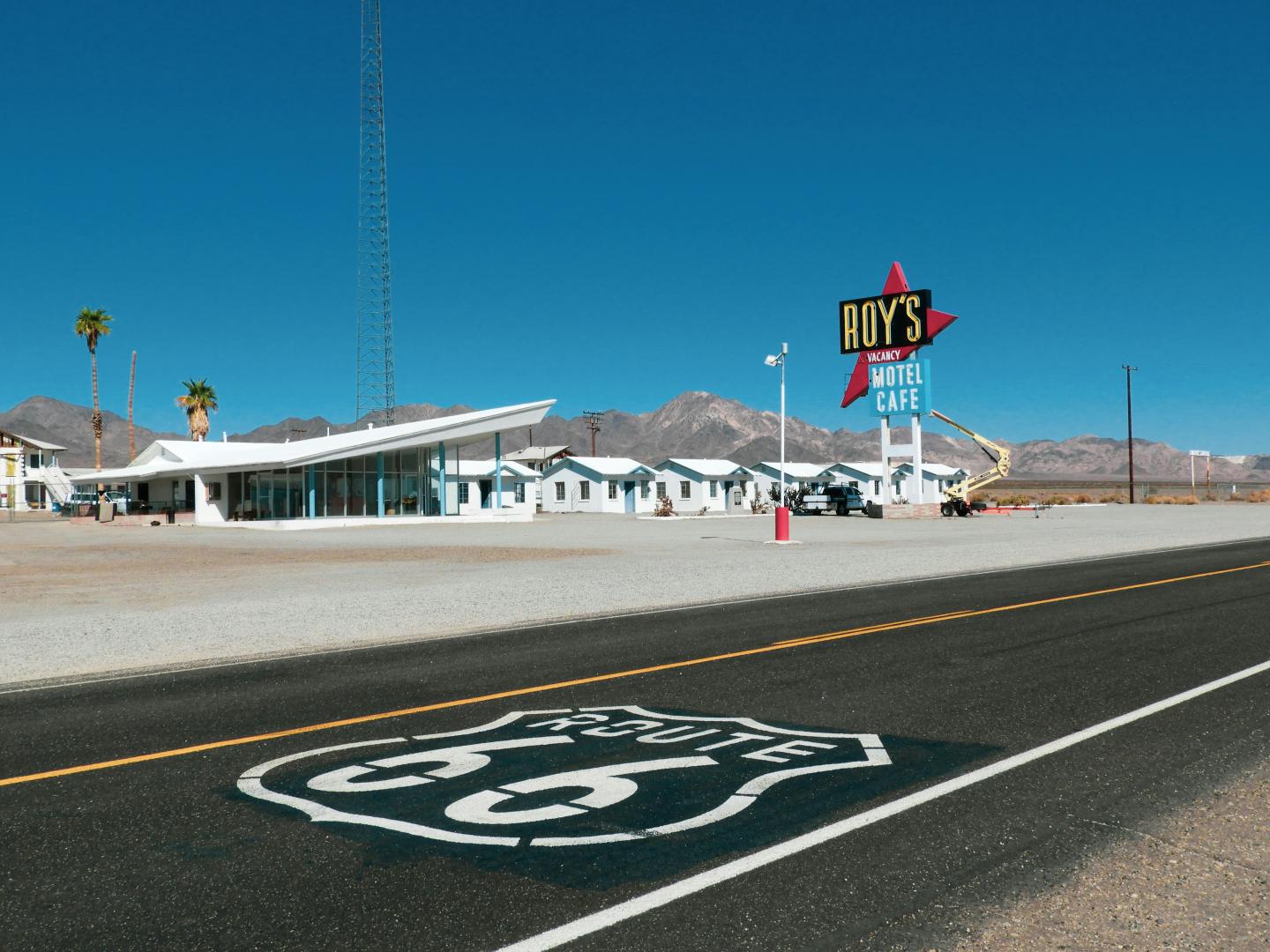Desert highway with a retro motel and palm trees under a clear blue sky.