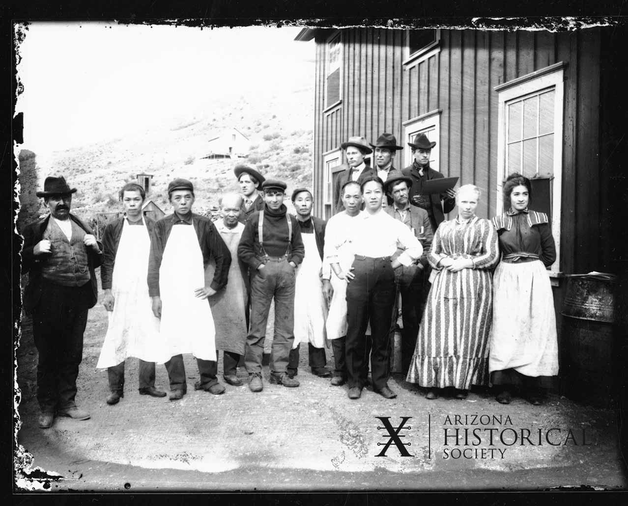 Historic black and white photograph of the kitchen Staff at the Clifton Hotel, Arizona, from the late 1800s, standing outside a wooden building.