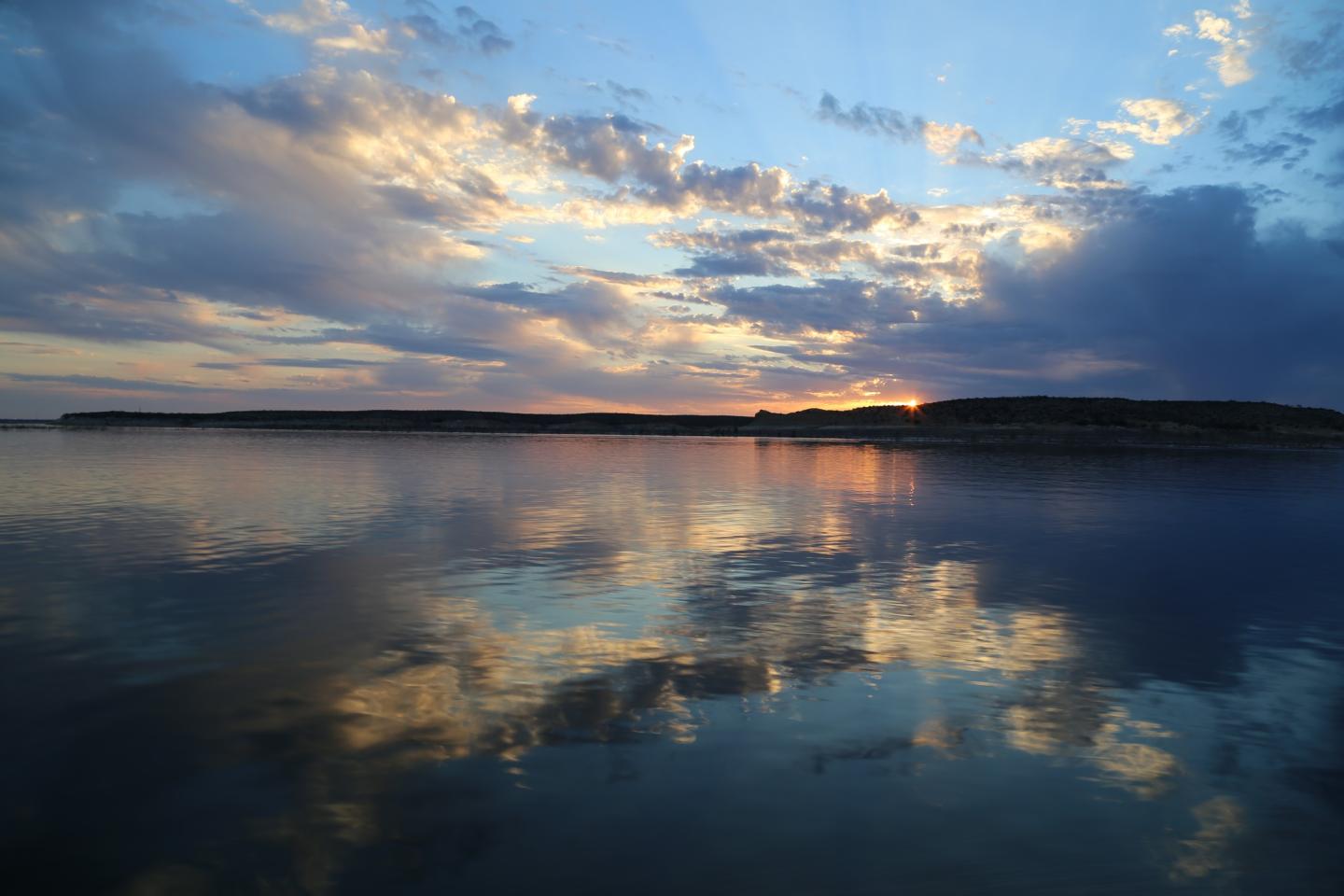 Sunset reflecting on calm lake, with clouds and blue sky.