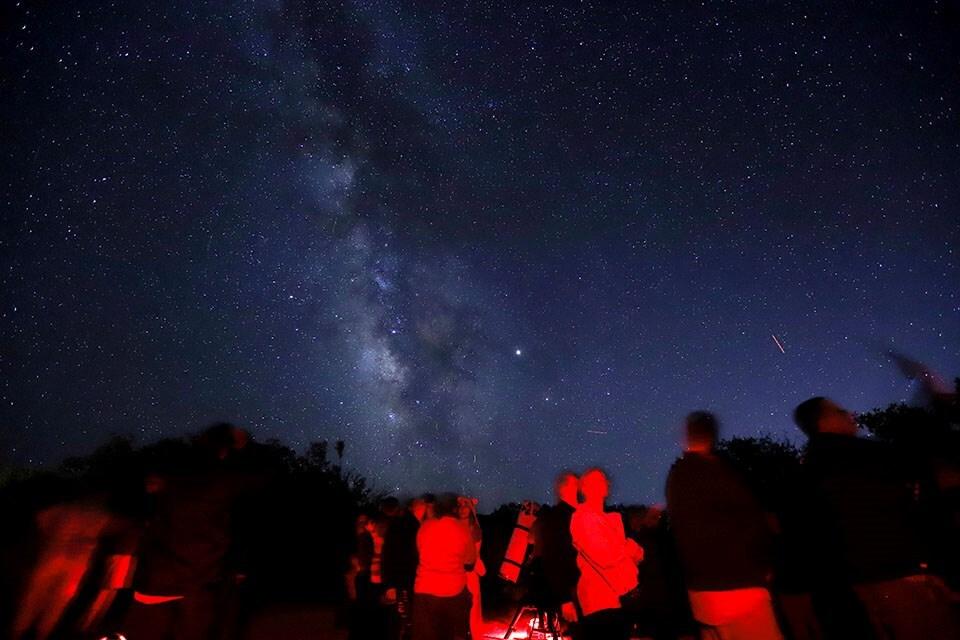 Starry night sky with the Milky Way; people silhouetted in red light.