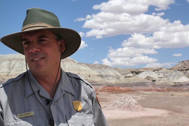 Park ranger in uniform with desert landscape and blue sky.