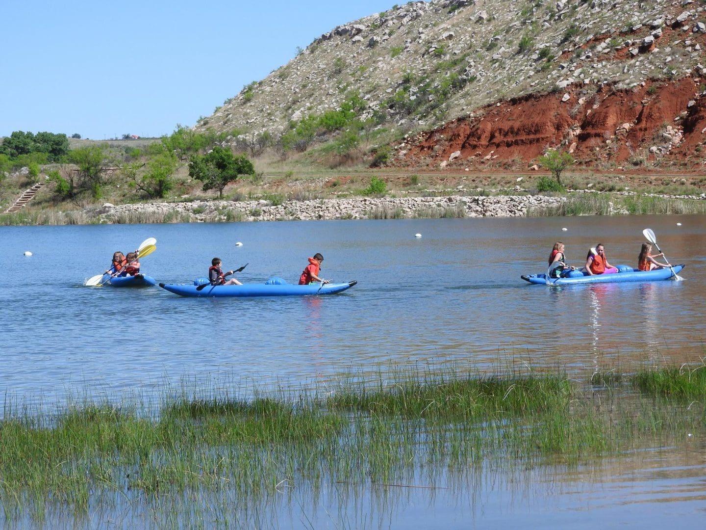 Kayakers paddling on a lake near a rocky hillside with clear blue skies.