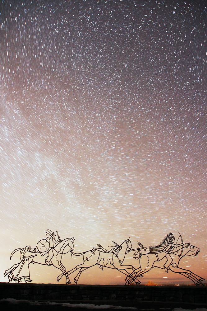 Stars over sculptures of galloping horses at dusk.