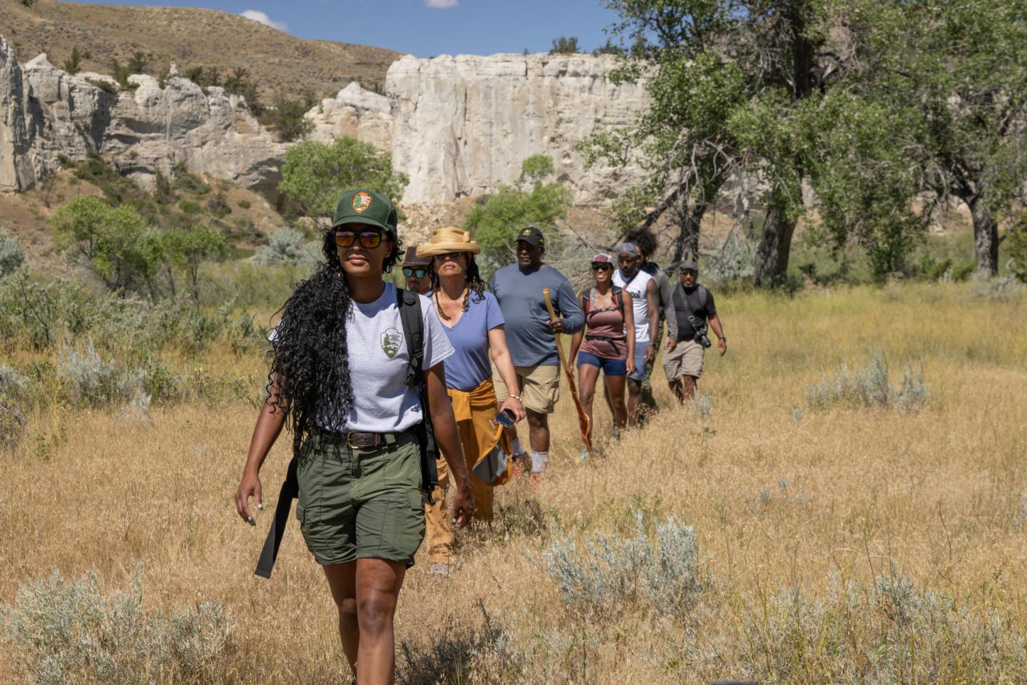 Park ranger leading a group hike through a grassy, rocky landscape.