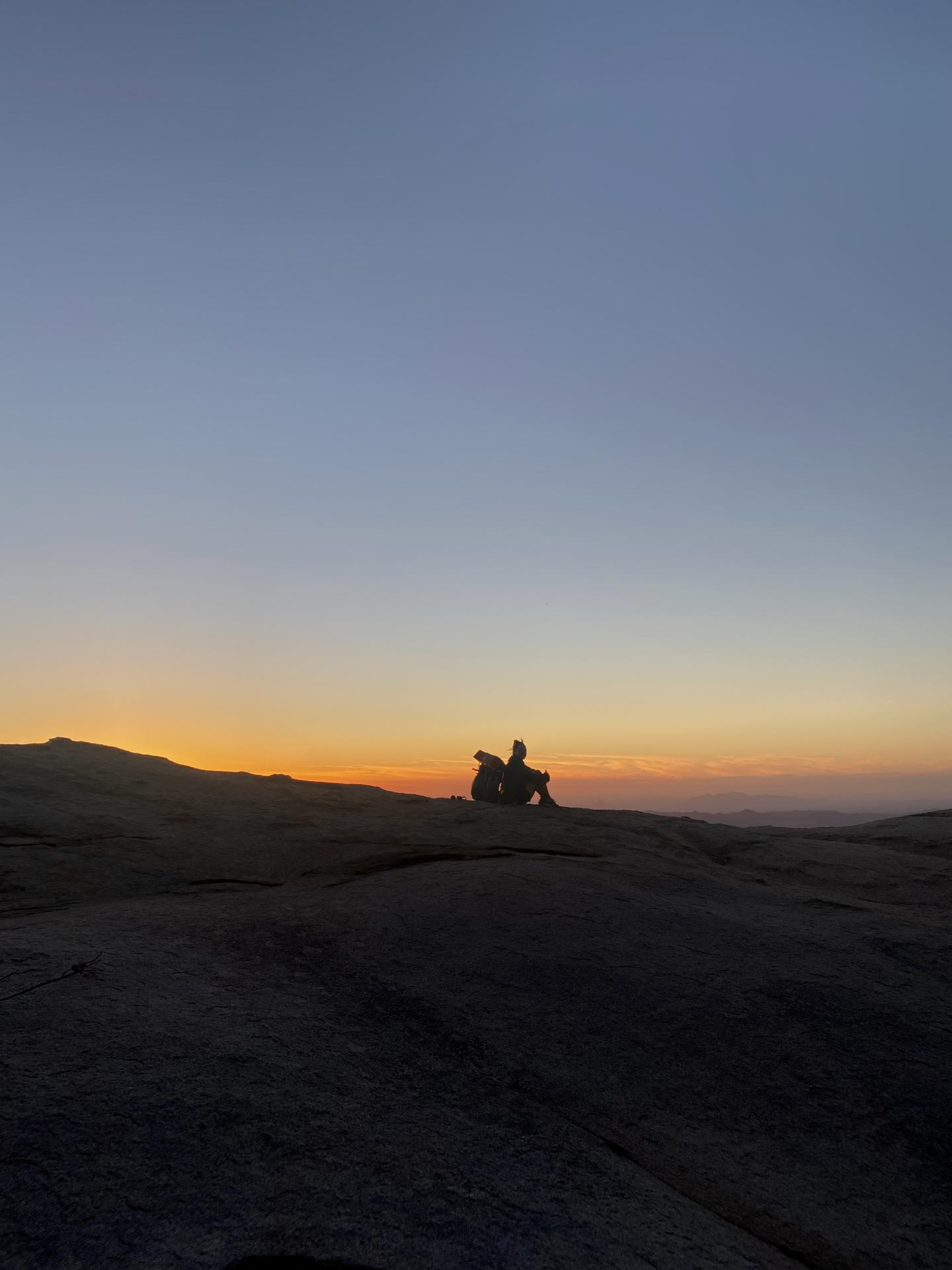 Silhouetted figures on a rocky hill at sunset.