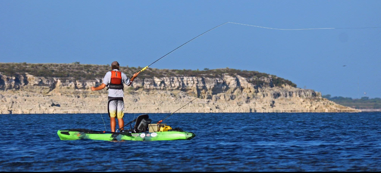 Person fishing on a kayak in blue water, with cliffs in the background.