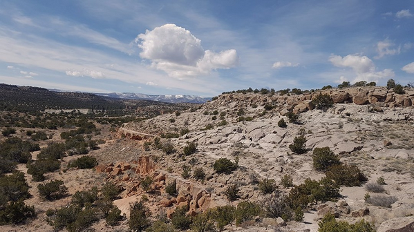 Rocky desert landscape under a cloudy blue sky with distant mountains.