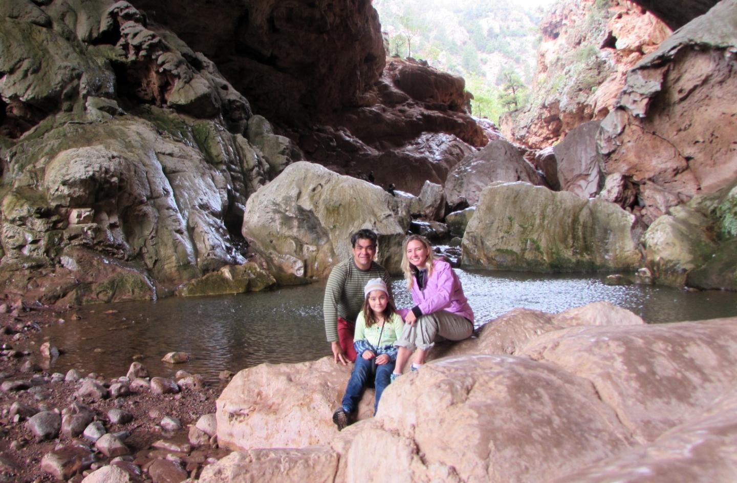 Family posing on rocks in a cave with a stream in the background.