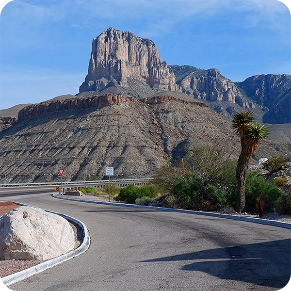 Road curving towards a mountain under a clear blue sky.