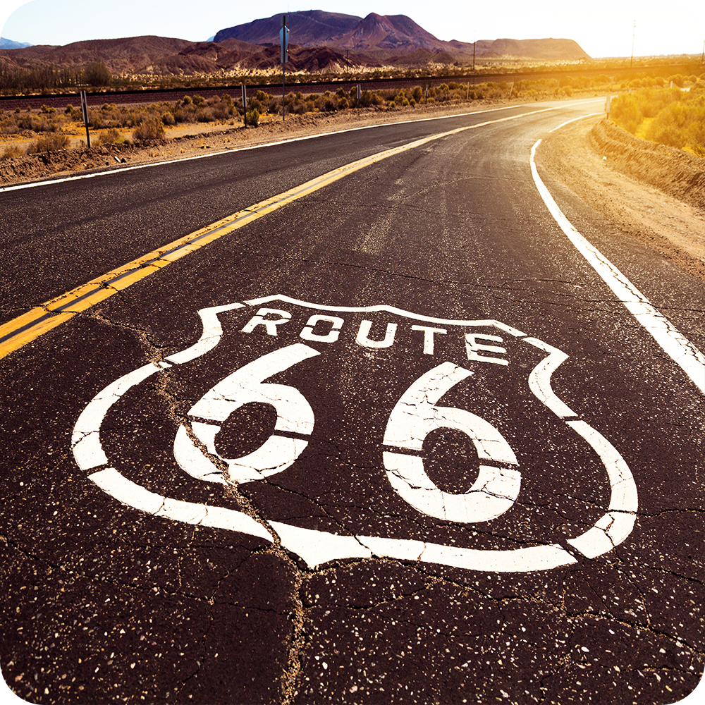 Curving Route 66 road at sunset with distant hills.