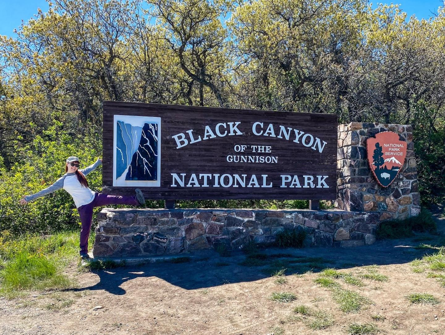 Person posing playfully by Black Canyon of the Gunnison National Park sign.