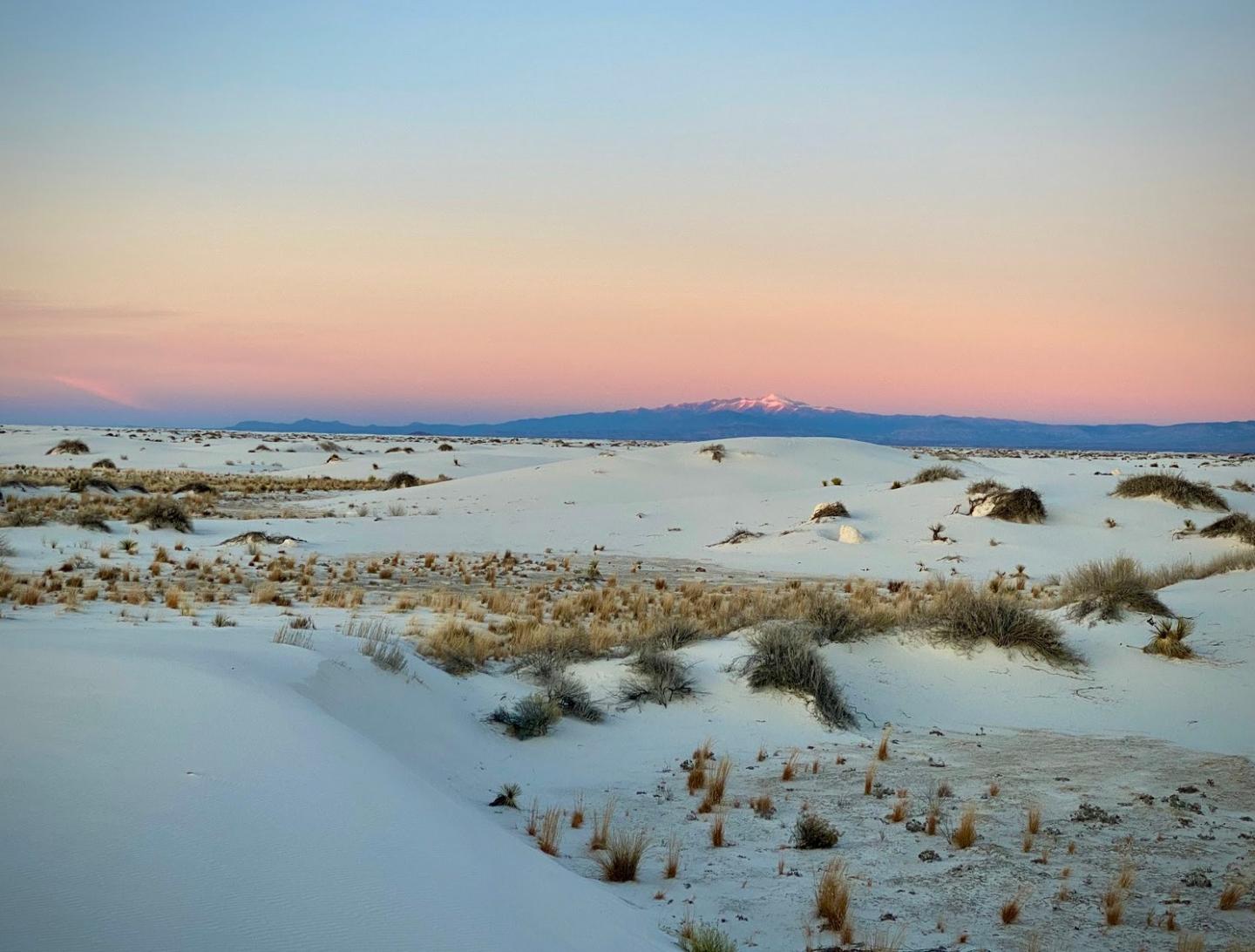 Desert landscape with white sand dunes under a pink and blue sky.