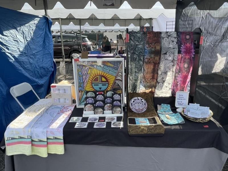 Market stall with colorful textiles and framed artwork on display.
