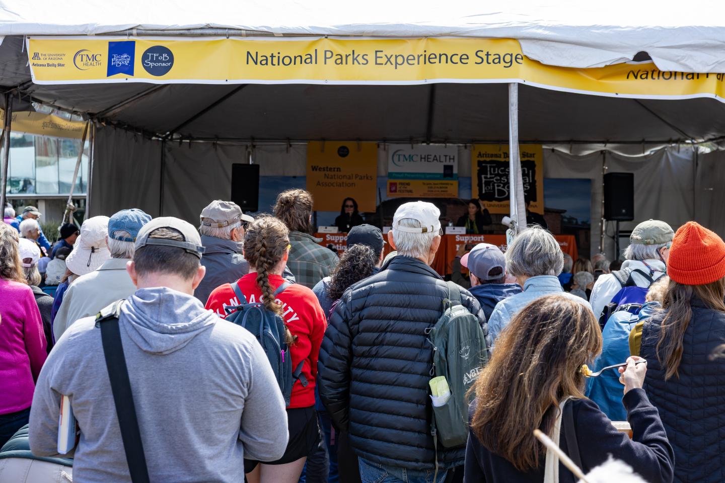 Crowd gathered under a tent at a National Parks event, listening to speakers on stage.