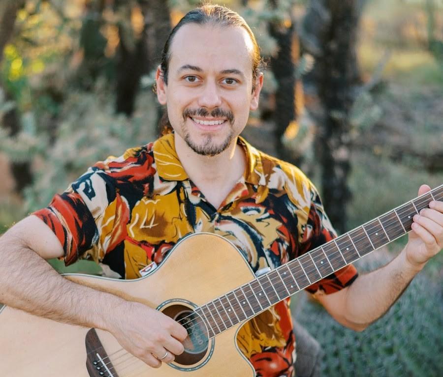 Man smiling while playing acoustic guitar outdoors.