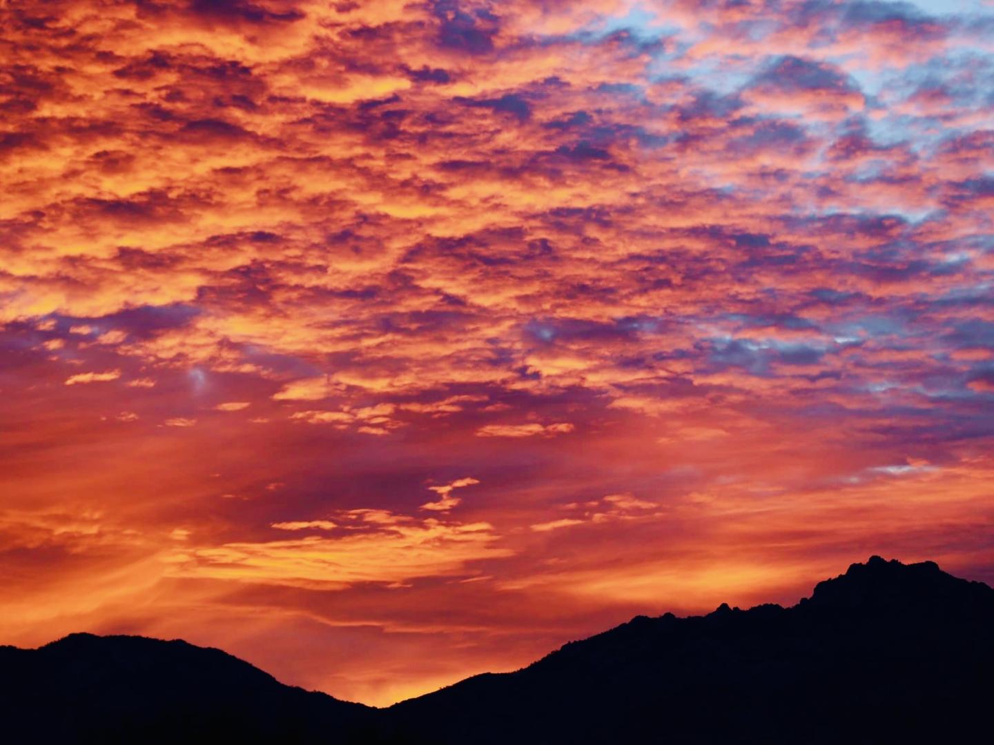 Fiery sunset with vibrant orange and purple clouds over silhouette of mountains.